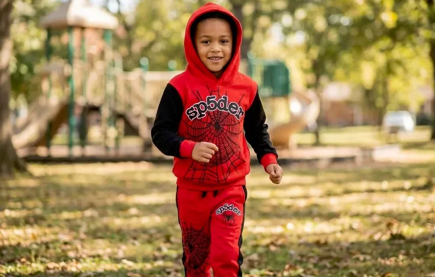 Happy child wearing red Kids Sp5der Tracksuit with spider web design playing outdoors in park