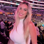 Kayla Simmons smiling at an NBA game courtside, wearing a white outfit at a basketball arena