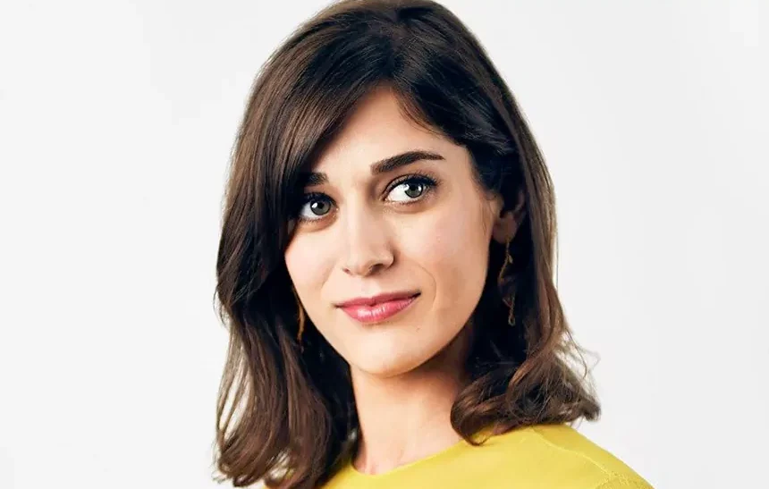 Lizzy Caplan net worth — actress in yellow top with brown hair against white background