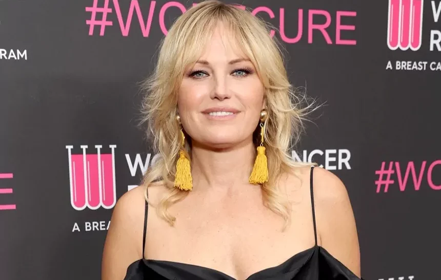 Malin Akerman at a breast cancer awareness event, smiling in a black dress with gold tassel earrings