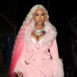 Stunna Girl net worth — rapper wearing pink fur coat and diamond chain necklace at a night event