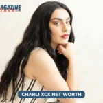 Charli XCX net worth photo: woman with long dark hair in striped dress