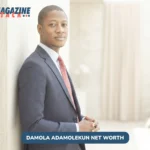 Damola Adamolekun in navy suit and red tie leaning against concrete wall