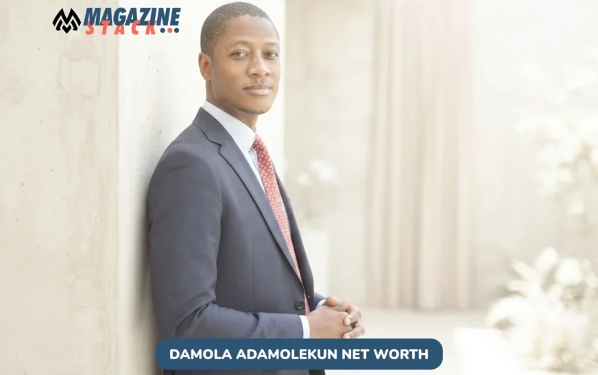 Damola Adamolekun in navy suit and red tie leaning against concrete wall